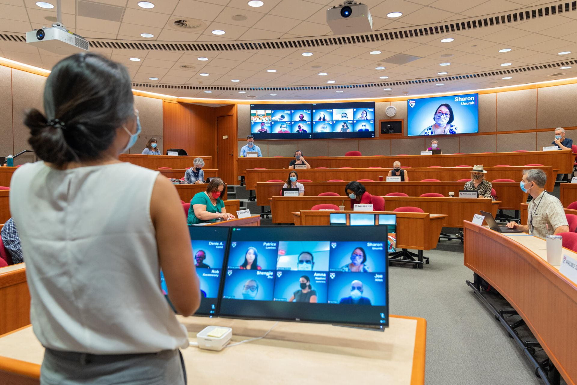 Woman stands before a monitor in a hybrid classroom.