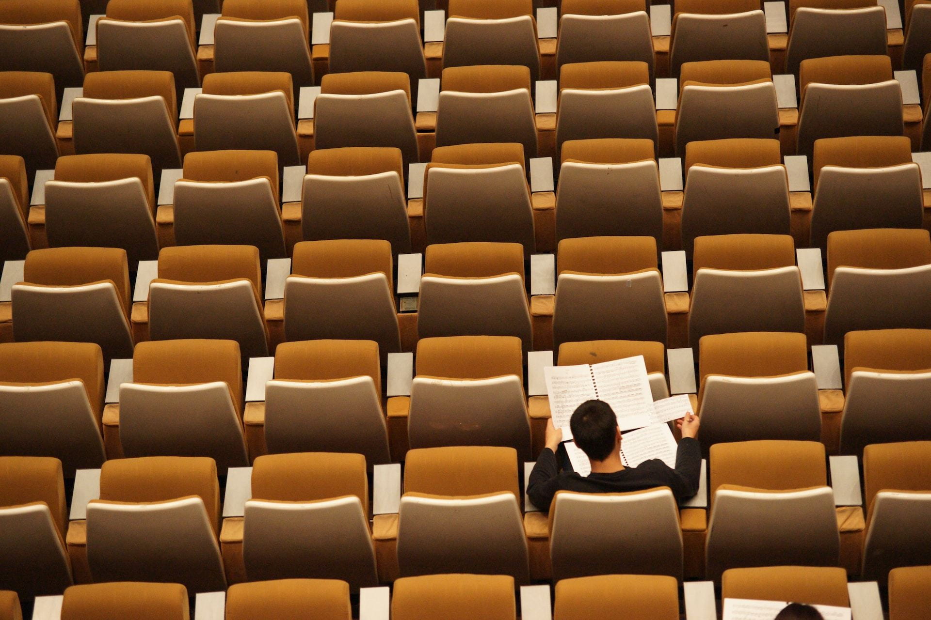 Aerial view of a man sitting alone in rows of lecture seating.